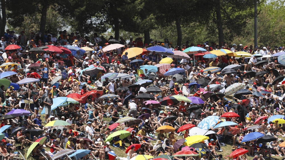 Auf den Zuschauerrängen schützen sich unzählige Zuschauer mit Sonnenschirmen vor der Hitze.