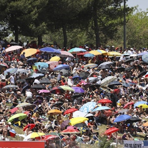 Auf den Zuschauerrängen schützen sich unzählige Zuschauer mit Sonnenschirmen vor der Hitze.