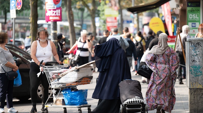 Eine Frau steht mit einem Einkaufswagen auf einem Gehweg in Köln.
