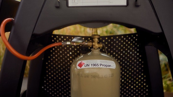Eine Flasche Gas ist an einen Gasgrill angeschlossen.