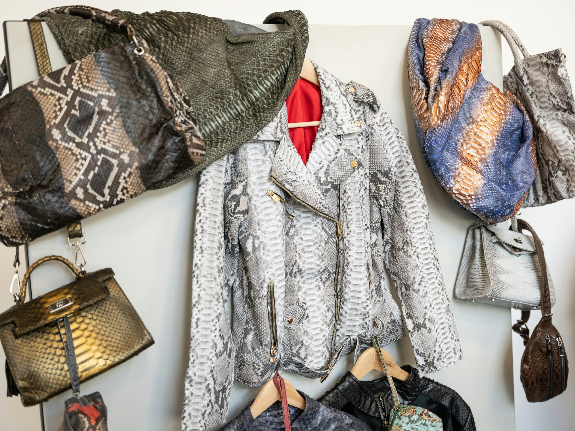 Kleidungsstücke und Taschen aus Python- beziehungsweise Krokodilleder hängen an einer Wand.