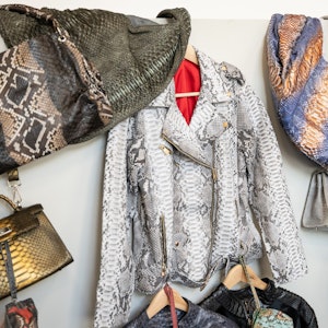Kleidungsstücke und Taschen aus Python- beziehungsweise Krokodilleder hängen an einer Wand.