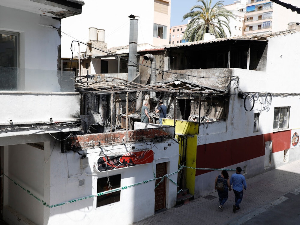Menschen gehen nach einem Brand am Restaurant «Why Not Mallorca?» vorbei. Die Polizei hat auf Mallorca 13 deutsche Urlauber festgenommen, weil sie den Brand ausgelöst haben sollen.