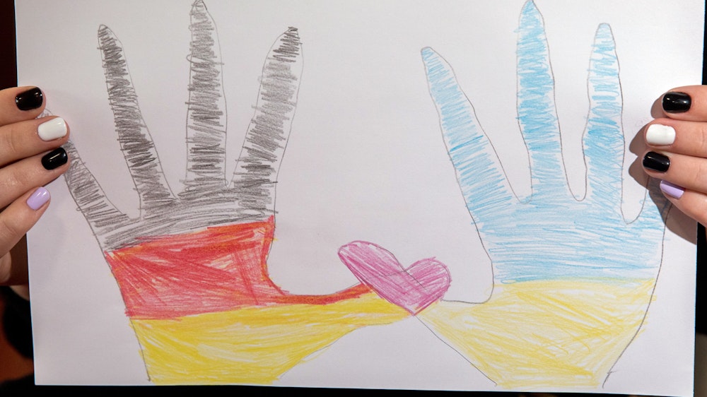Zwei von Kindern gemalte Hände, eine in deutschen und eine in ukrainischen Farben, formen mit ihren Daumen ein rosa Herz.