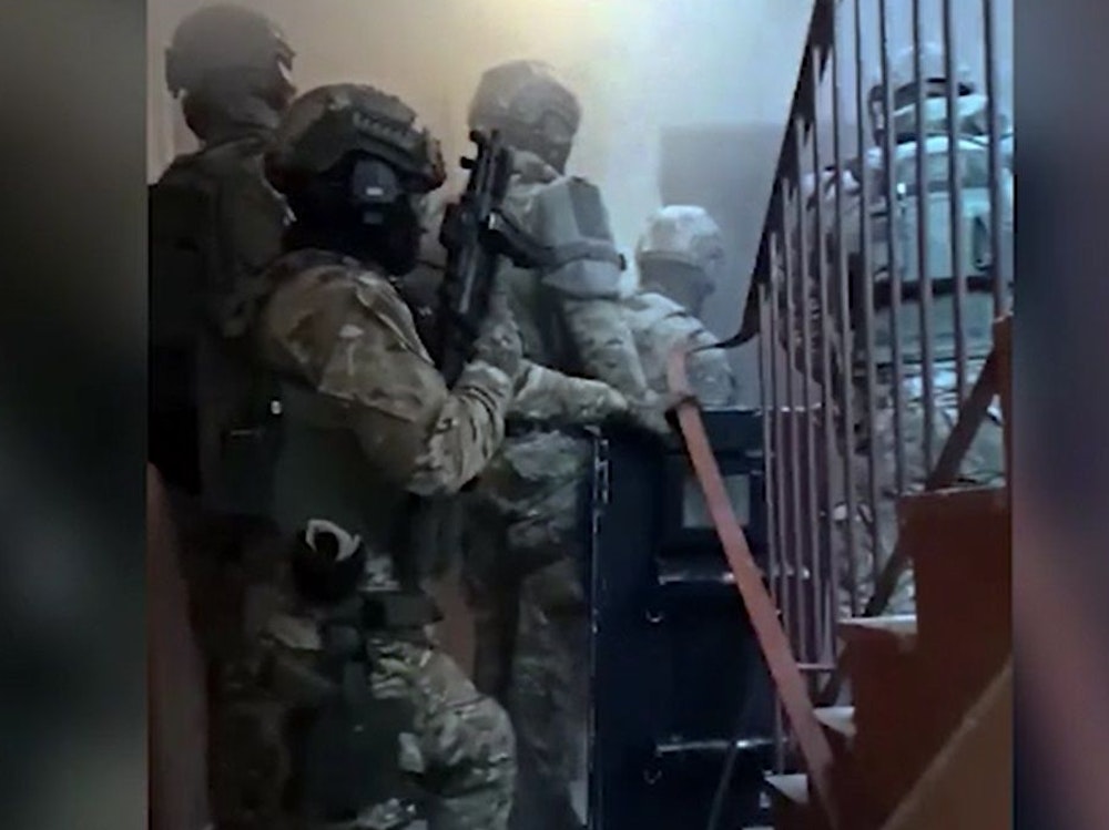 Vermummte Spezialkräfte stehen in einem Treppenhaus vor einer Wohnung, die sie gleich stürmen.