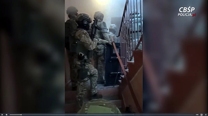 Vermummte Spezialkräfte stehen in einem Treppenhaus vor einer Wohnung, die sie gleich stürmen.