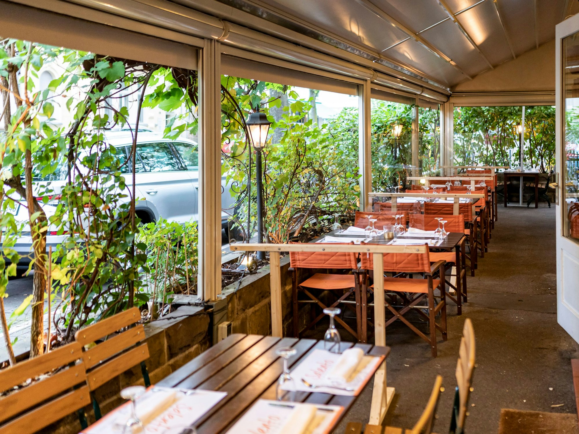 Kübel mit großen Pflanzen grenzen die Außengastronomie eines Restaurants vom Bürgersteig ab.