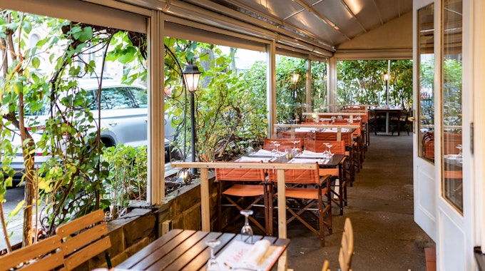 Kübel mit großen Pflanzen grenzen die Außengastronomie eines Restaurants vom Bürgersteig ab.