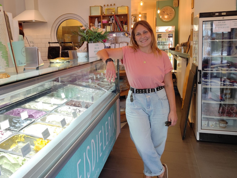 Ladeninhaberin Michaela Staffel lehnt sich lächelnd an die Eistheke der "Eisdielerin".
