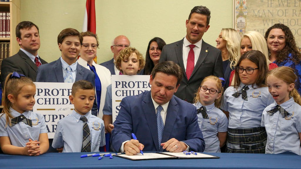 Gouverneur Ron DeSantis unterzeichnet ein Gesetz in Florida. Um ihn stehen mehrere Schülerinnen und Schüler.