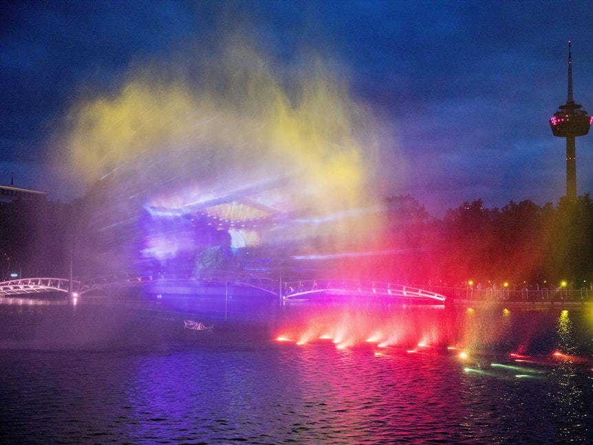 Bunte Lichteffekte auf dem Wassernebel über dem See im Kölner Mediapark.