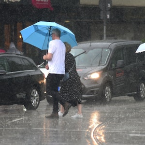 Menschen laufen in Köln mit Regenschirmen über die nassen Straßen.