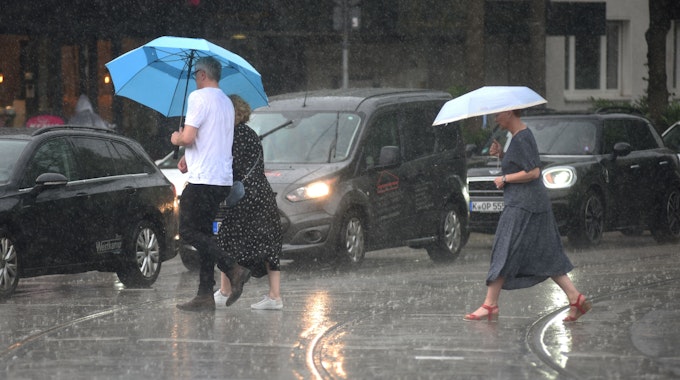 Menschen laufen in Köln mit Regenschirmen über die nassen Straßen.