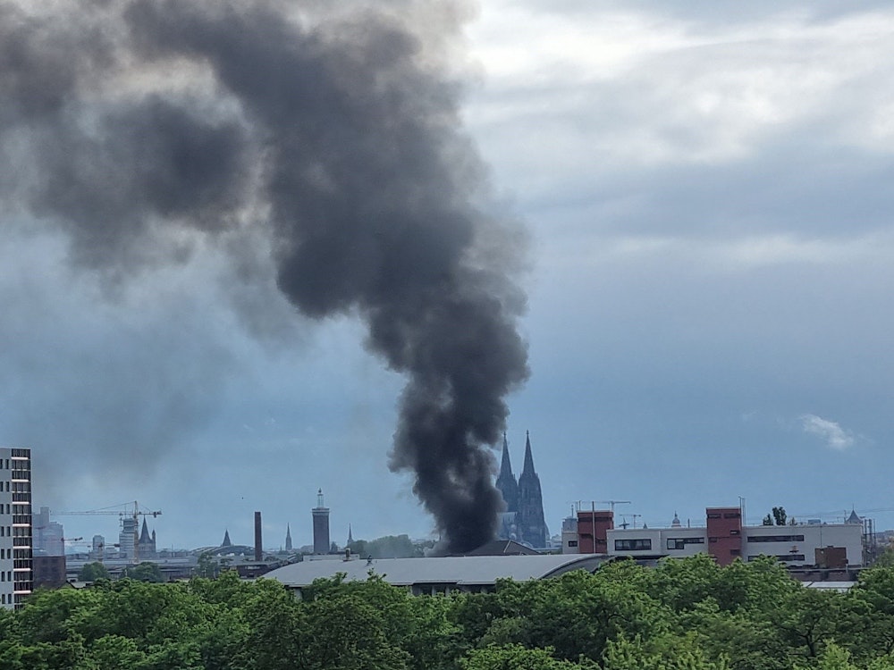 Eine Lagerhalle in Köln-Mülheim brennt. Die Rauchwolke ist noch von weit her zu sehen.