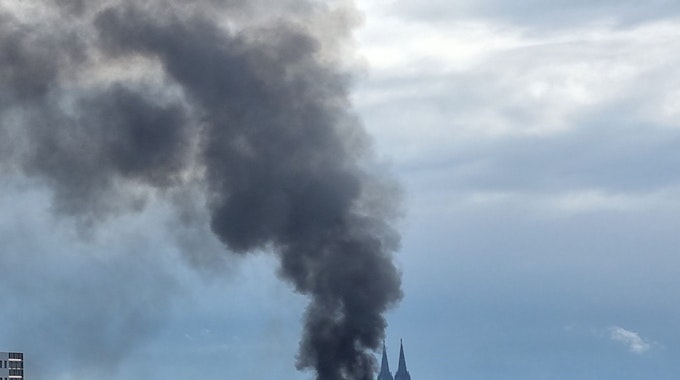 Eine Lagerhalle in Köln-Mülheim brennt. Die Rauchwolke ist noch von weit her zu sehen.