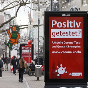 Menschen gehen an einer elektronischen Werbetafel mit der Aufschrift "Positiv getestet?" in der Kölner Innenstadt vorbei.