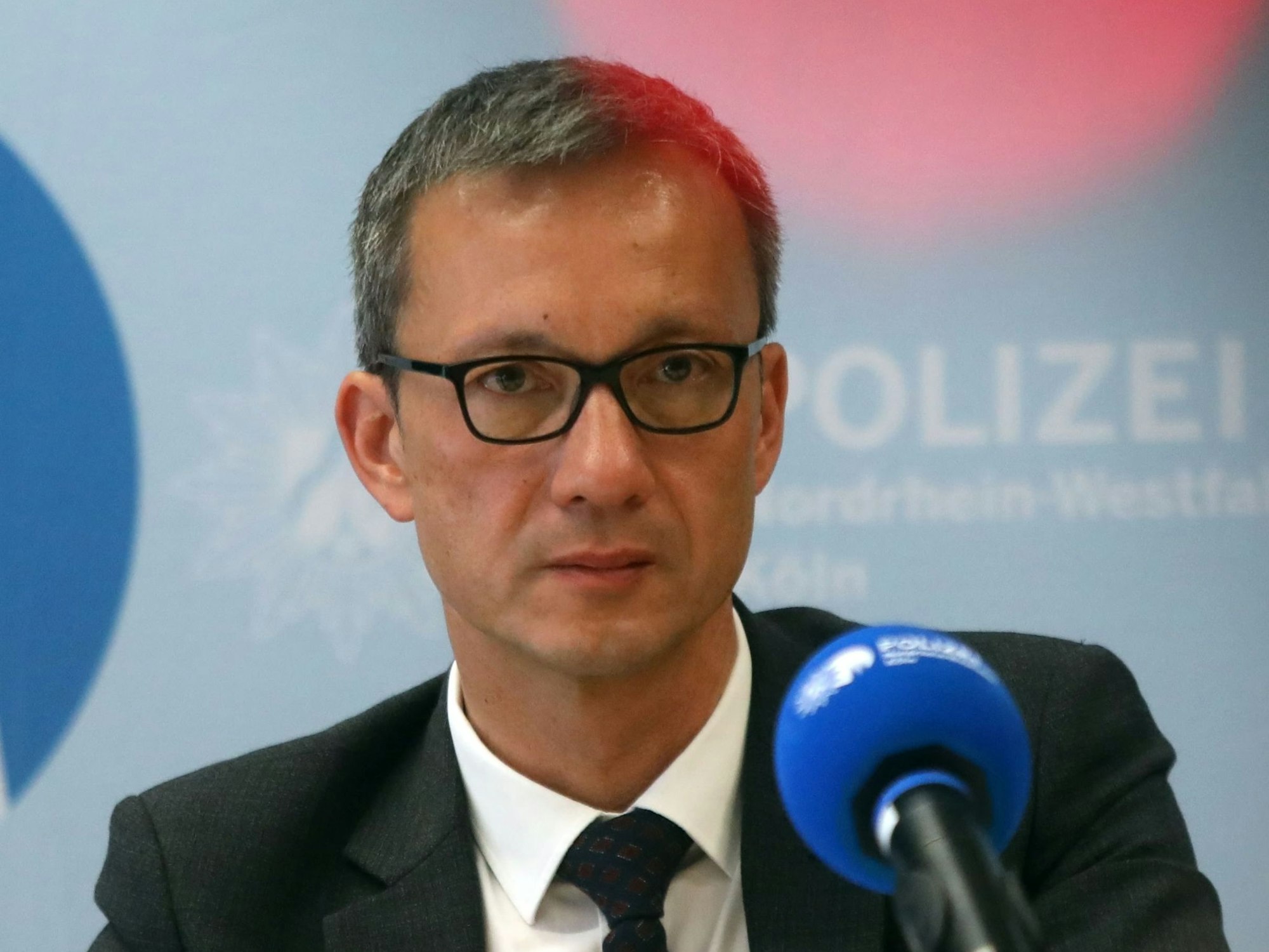 Der Kölner Polizeipräsident Falk Schnabel sitzt auf einem Podium vor einem Mikrofon.