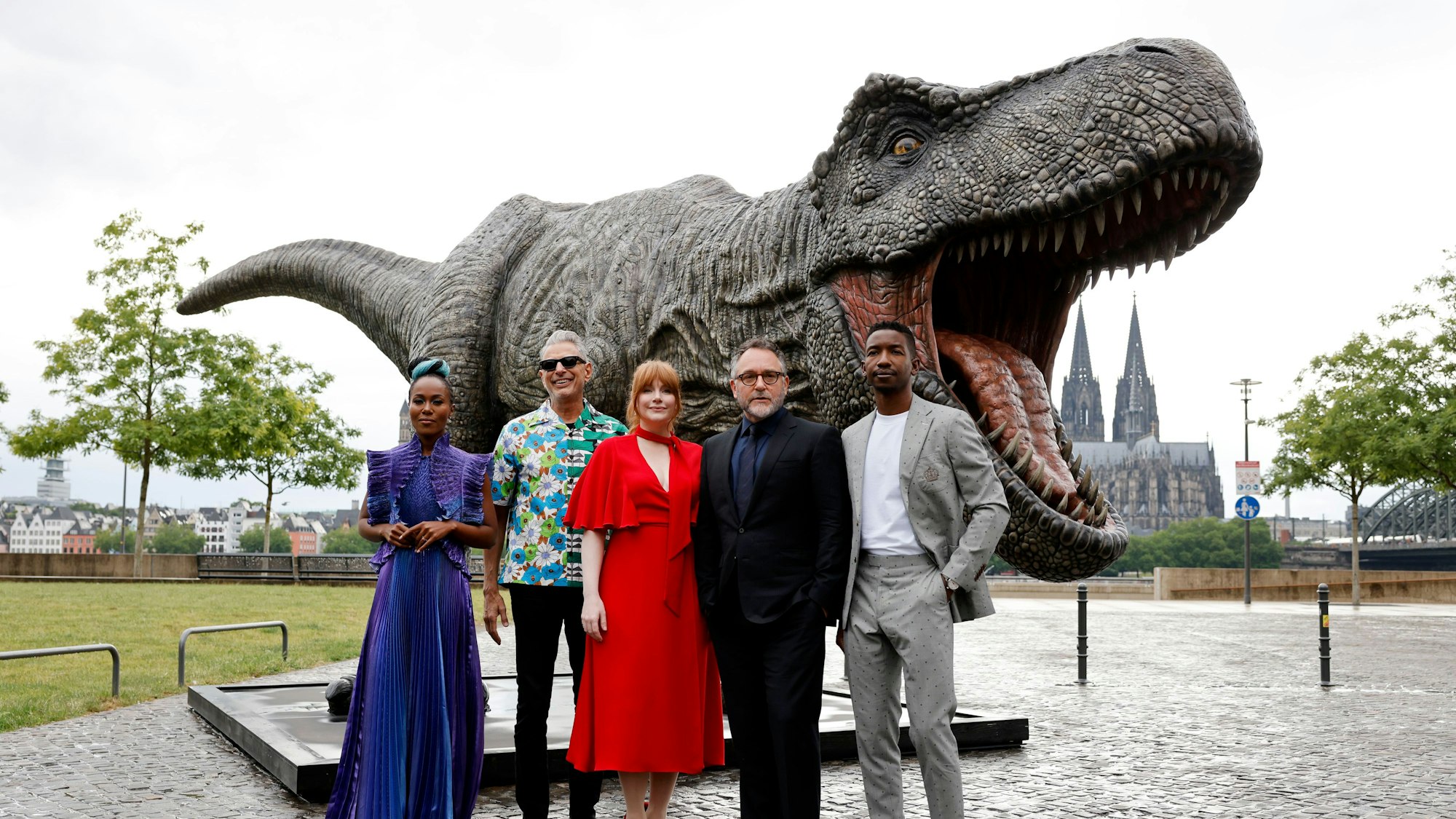 Die Schauspieler DeWanda Wise (v.l.), Jeff Goldblum, Bryce Dallas Howard, Regisseur Colin Trevorrow und Mamoudou Athie stehen vor einer T-Rex Figur. 
