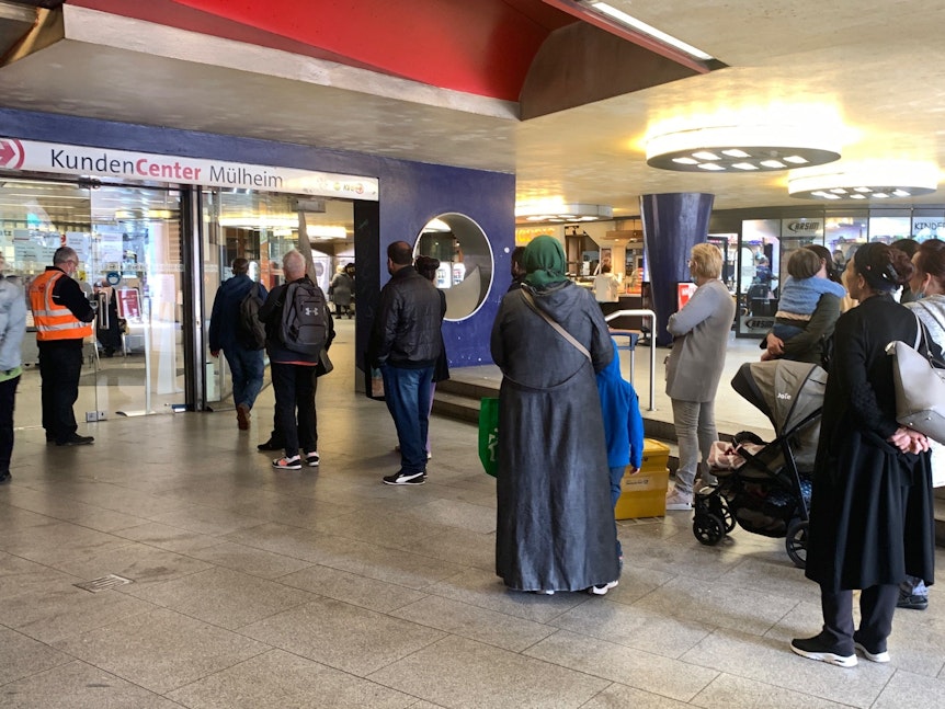 Vor dem KVB-Kundencenter in Köln-Mülheim warten Menschen in einer langen Schlange vor dem Eingang.