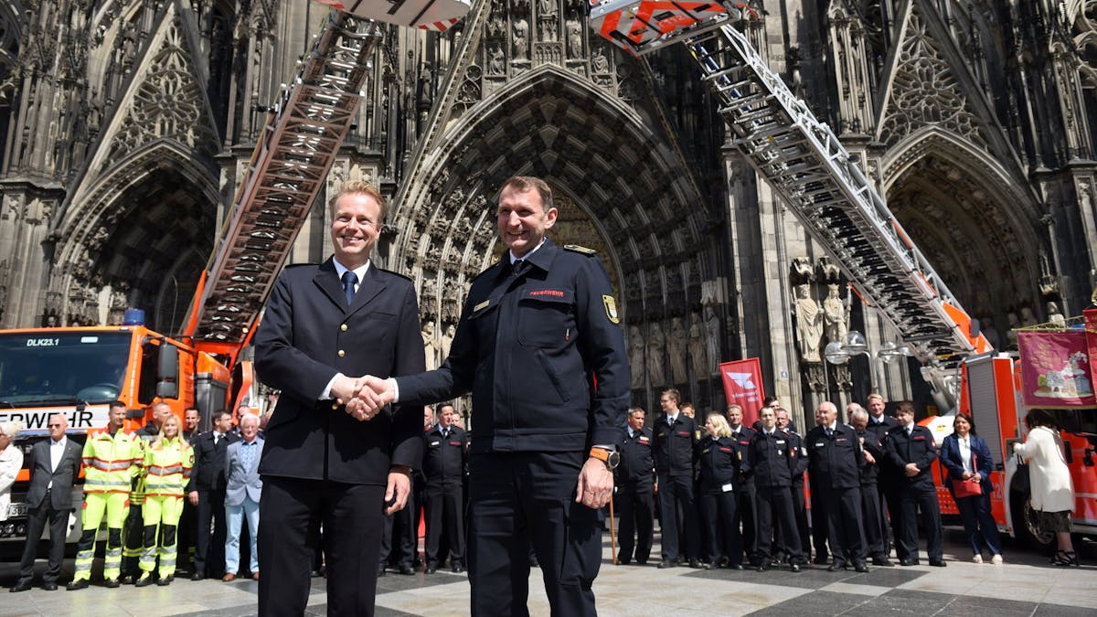 Kräfte sowie Einsatzfahrzeuge der Feuerwehren Köln und Düsseldorf präsentieren sich auf der Domplatte, im Vordergrund schütteln sich die Chefs die Hand.&nbsp;