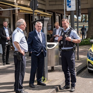 Innenminister Herbert Reul im Gespräch mit zwei Polizisten vor einem Streifenwagen am Neumarkt.