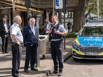 Innenminister Herbert Reul im Gespräch mit zwei Polizisten vor einem Streifenwagen am Neumarkt.