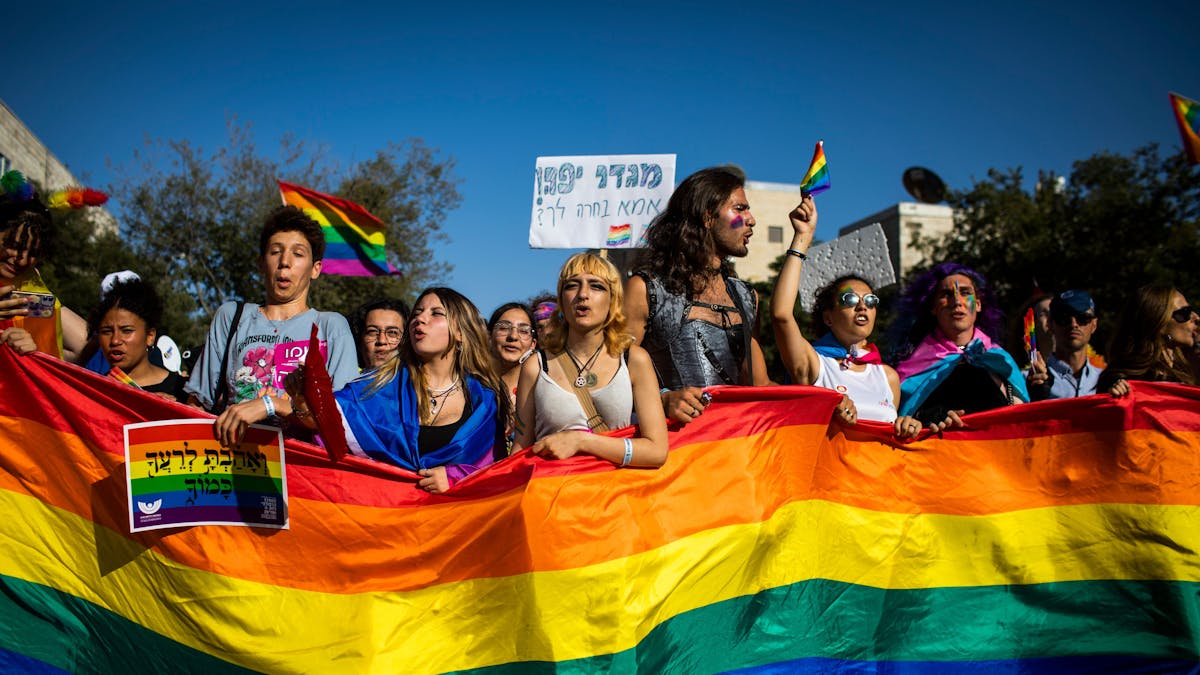 Menschen marschieren mit Regenbogenfahnen und Schildern während der jährlichen Gay-Pride-Parade durch die Straßen.