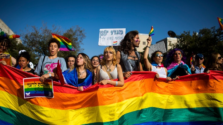 Menschen marschieren mit Regenbogenfahnen und Schildern während der jährlichen Gay-Pride-Parade durch die Straßen.