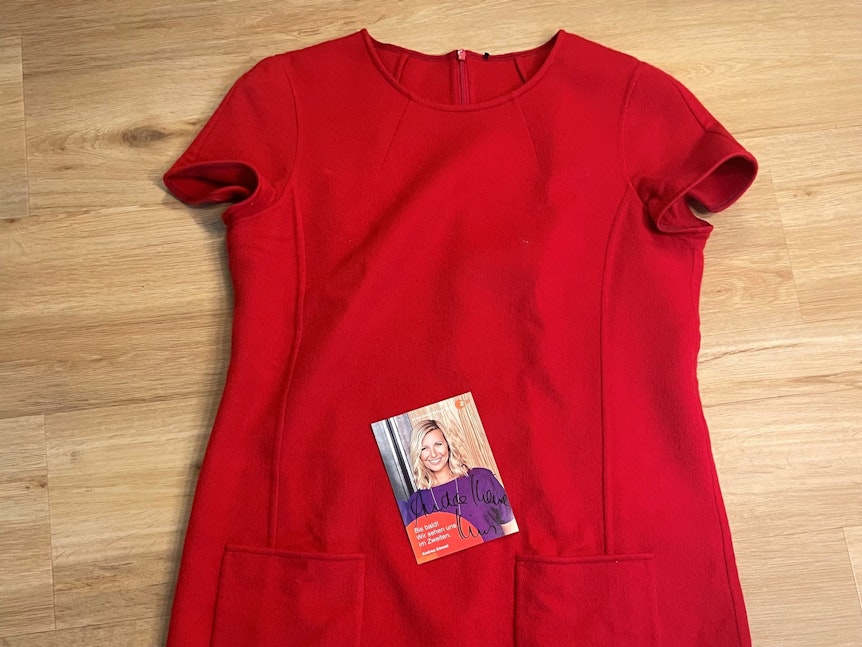 Ein kurzärmliges, rotes Kleid und eine Autogrammkarte liegen auf dem Boden.