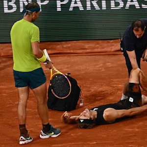 Alexander Zverev liegt schreiend am Boden, während ihn ein Arzt behandelt. Gegenspieler Rafael Nadal leidet daneben mit.