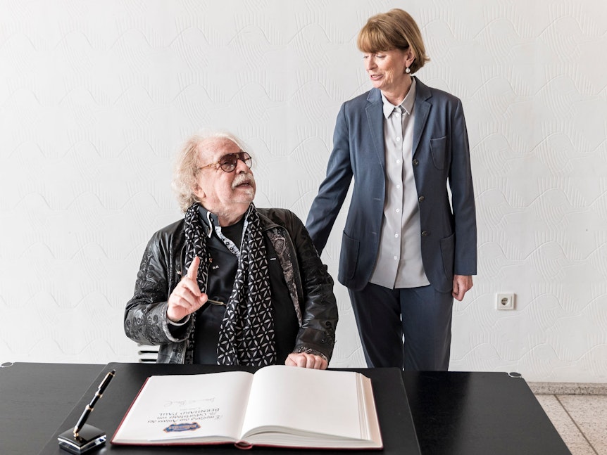 Bernhard Paul trägt sich in ein Buch ein, Henriette Reker steht daneben.