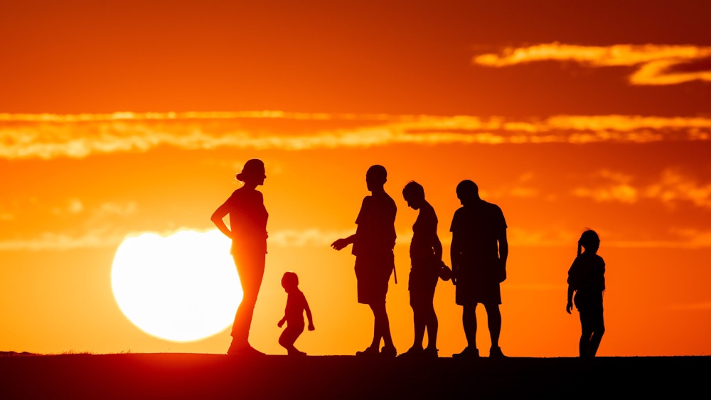 Menschen stehen zusammen vor der untergehenden Sonne. Ob groß oder klein: Die Körpergröße einer Person erhöht das Risiko für bestimmte Krankheiten.