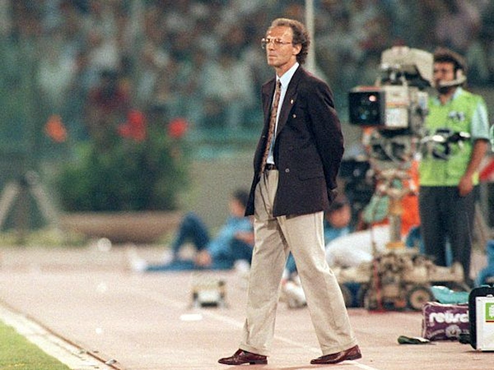 Beckenbauer verfolgt das Spiel stehend am Spielfeldrand.