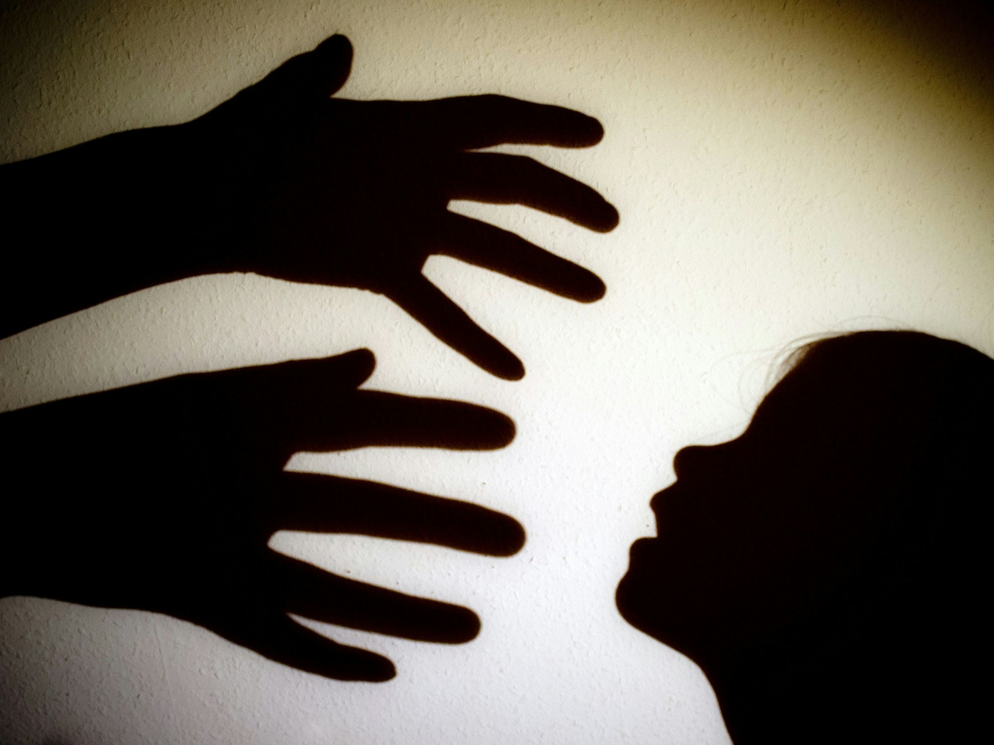Schatten von Händen einer erwachsenen Person und dem Kopf eines Kindes sind an einer Wand eines Zimmers zu sehen.
