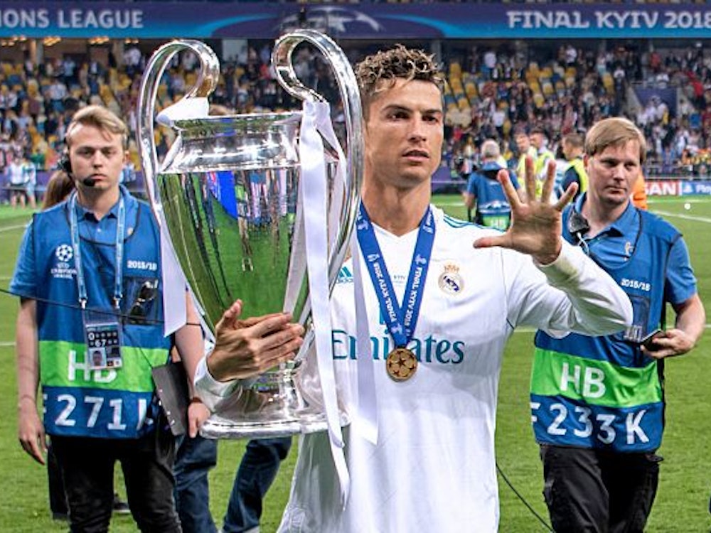 Ronaldo hält den Champions League auf seinem rechten Arm und zeigt mit der linken Fünf.