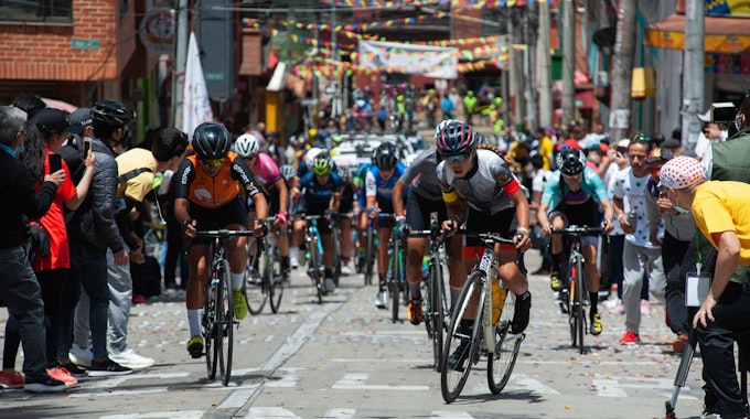 Die Rad-Profis kämpfen sich bei der Vuelta a Colombia auf einer schmalen Gasse den Berg hoch – Fans feuern von allen Seiten an.