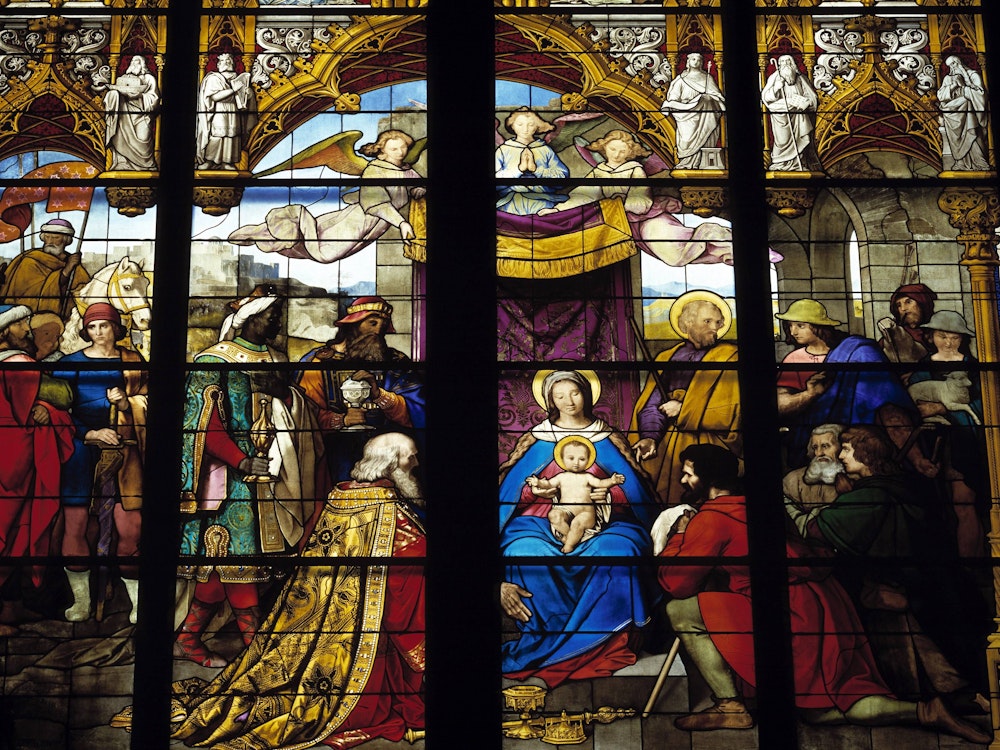 Ein bunt bemaltes Glasfenster im Kölner Dom, das die Ankunft der heiligen drei Könige darstellt.