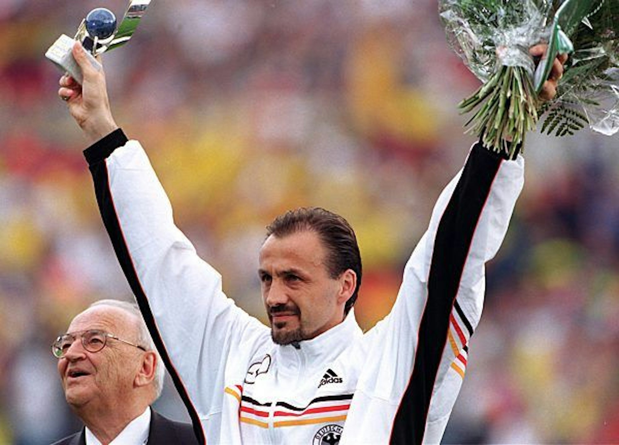 Jürgen Kohler hält einen Blumenstrauß und einen Pokal hoch und bedankt sich bei den Zuschauern.