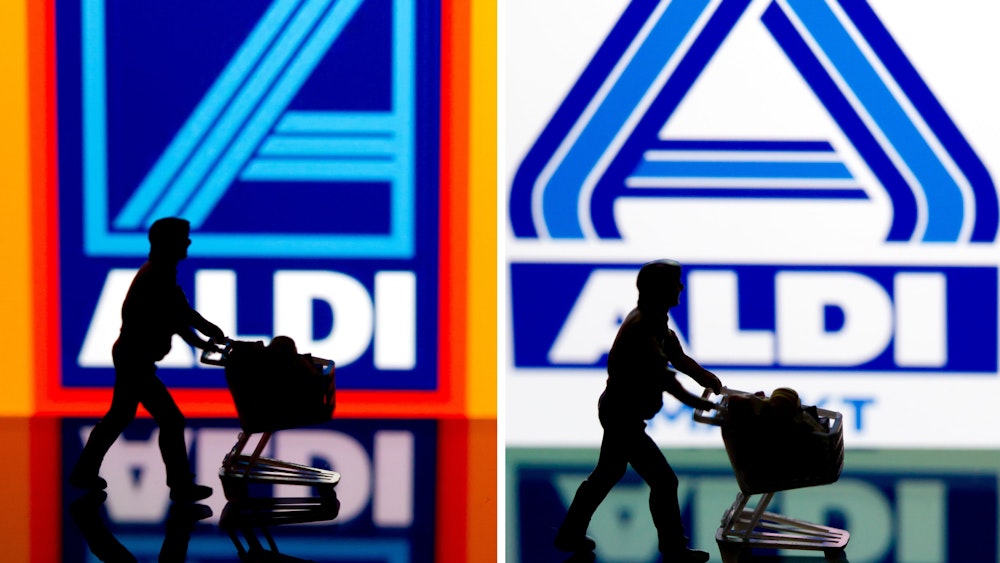 Eine kleine Plastikfigur mit einem Einkaufswagen in Berlin vor einem Logo von Aldi Süd (links) und Aldi Nord