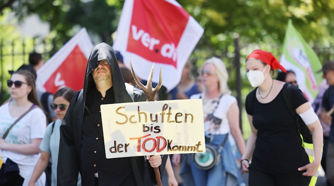 Mitarbeiterinnen und Mitarbeiter der Uniklinik laufen während einer Demonstration am 14. Juni 2022 mit einem Transparent mit der Aufschrift „Schuften bis der Tod kommt“ durch Bonn.