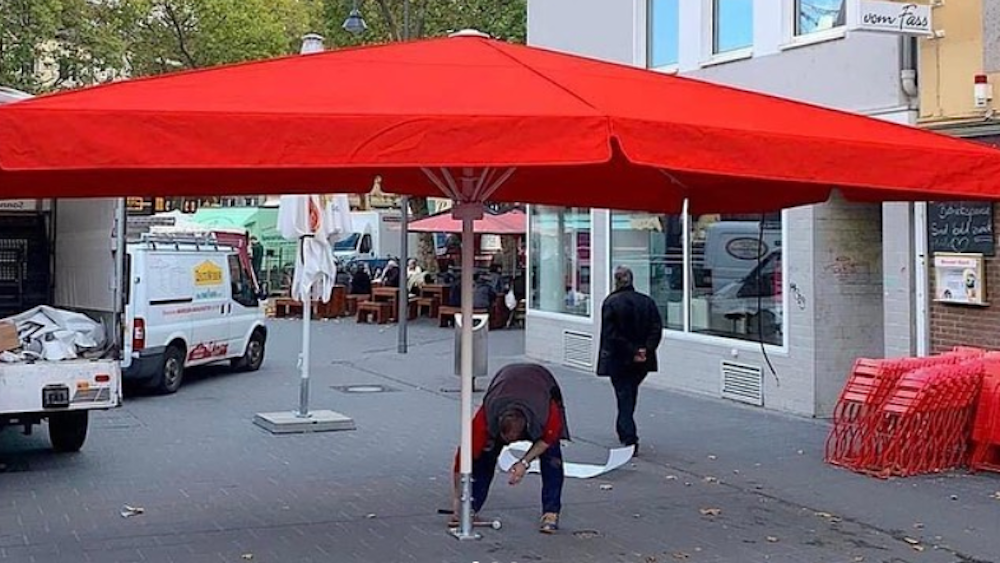 Ein Mann stellt einen großen roten Schirm auf dem Chlodwigplatz auf.