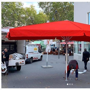 Ein Mann stellt einen großen roten Schirm auf dem Chlodwigplatz auf.