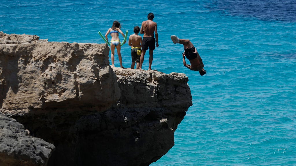 Menschen springen am Felsenstrand von Maioris an der Südostküste Mallorcas ins Meer.