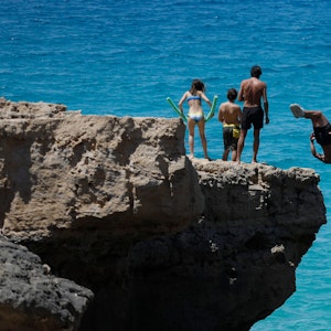 Menschen springen am Felsenstrand von Maioris an der Südostküste Mallorcas ins Meer.