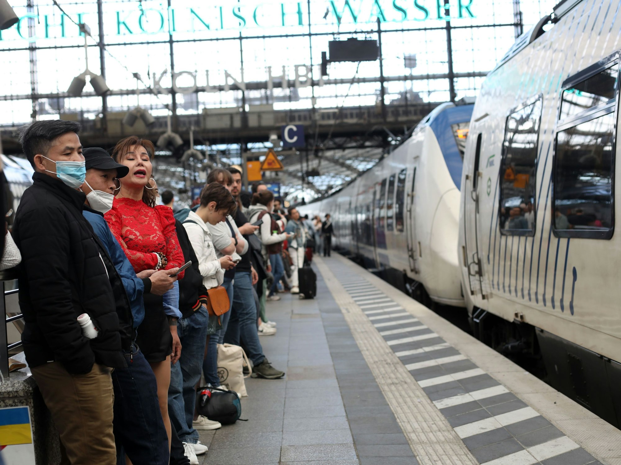 Menschen stehen am Hauptbahnhof in Köln am Gleis, während ein Zug einfährt.