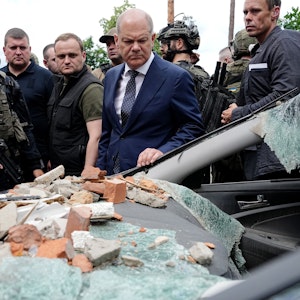 Bundeskanzler Olaf Scholz (M, SPD) blickt bei seinem Besuch auf ein stark beschädigtes Auto in Irpin im Großraum Kyjiw.