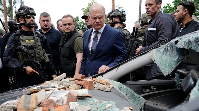 Bundeskanzler Olaf Scholz (M, SPD) blickt bei seinem Besuch auf ein stark beschädigtes Auto in Irpin im Großraum Kyjiw.