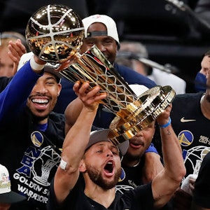Stephen Curry stemmt vor seinen feiernden Kollegen die NBA-Trophäe in die Luft.