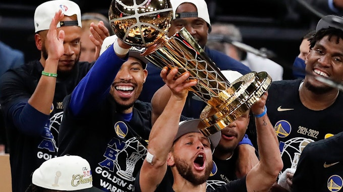 Stephen Curry stemmt vor seinen feiernden Kollegen die NBA-Trophäe in die Luft.