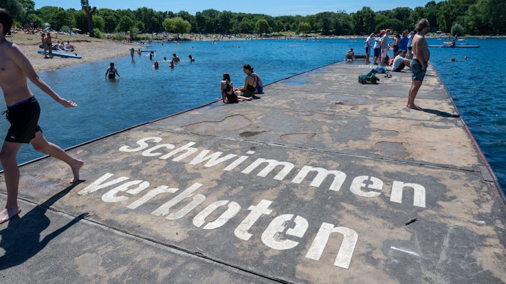 Auf dem Boden steht „Schwimmen verboten“. Trotzdem sind viele Menschen im Wasser.